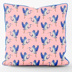 Flat shot of cotton cushion, pale pink base with repeating blue feathered heron pattern, blue edge piping
