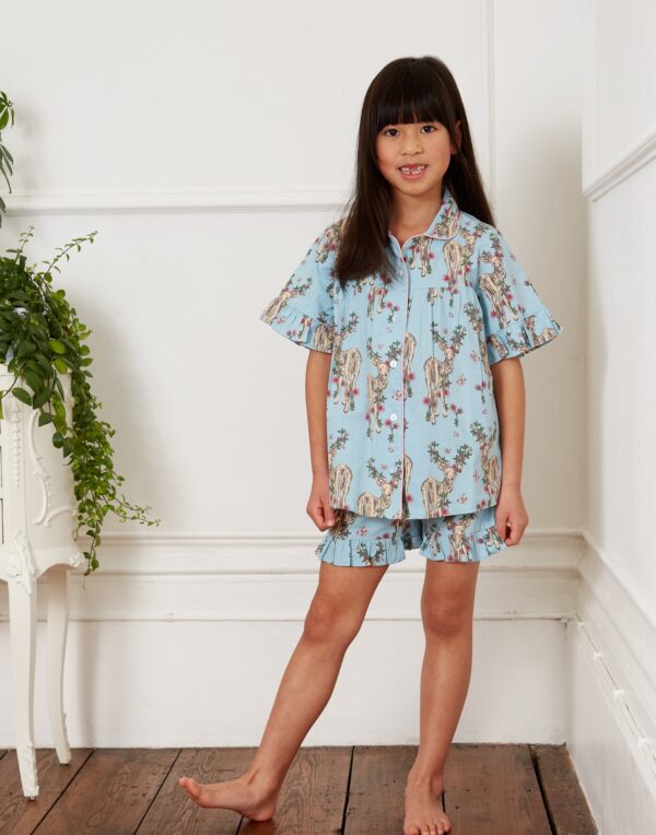 Child model wears kids cotton, shirt and shorts pjs, pale blue base with doe and floral antler pattern, frilled hems