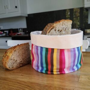 Bread basket rainbowon a kitchen wooden work top with bread in it and beside it, kitchen units in the background